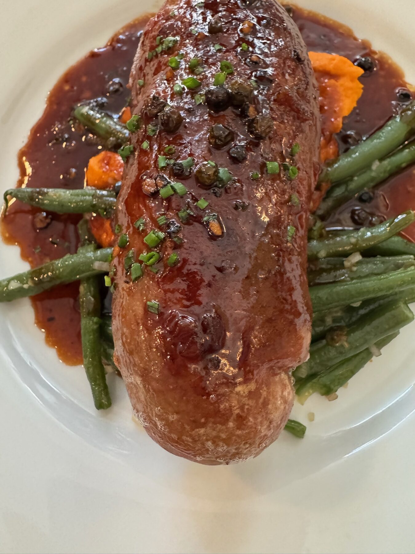 A large glazed sausage in a dark sauce with green beans and carrot puree