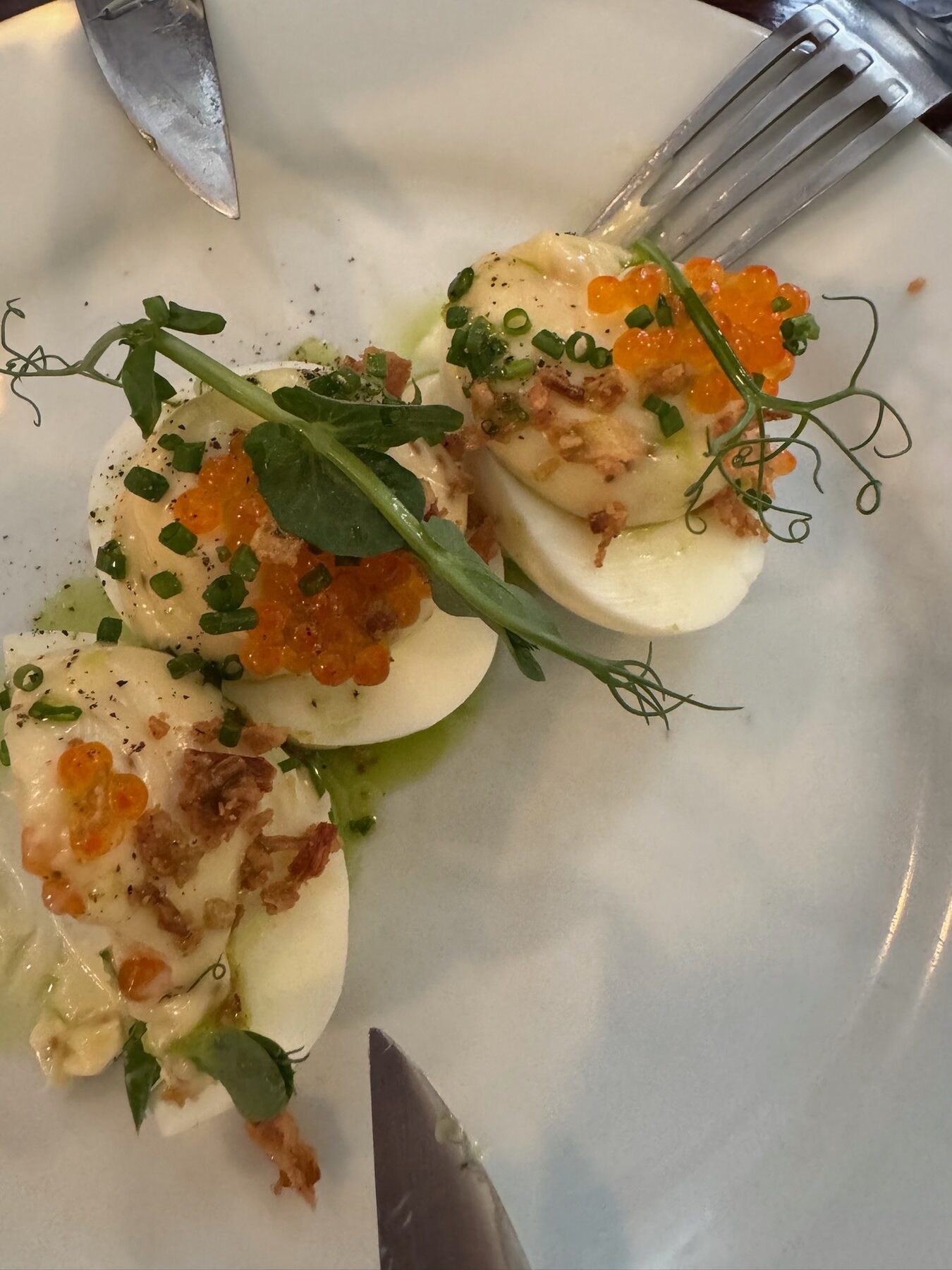 Halved eggs topped with orange roe, herbs and microgreens on a white plate