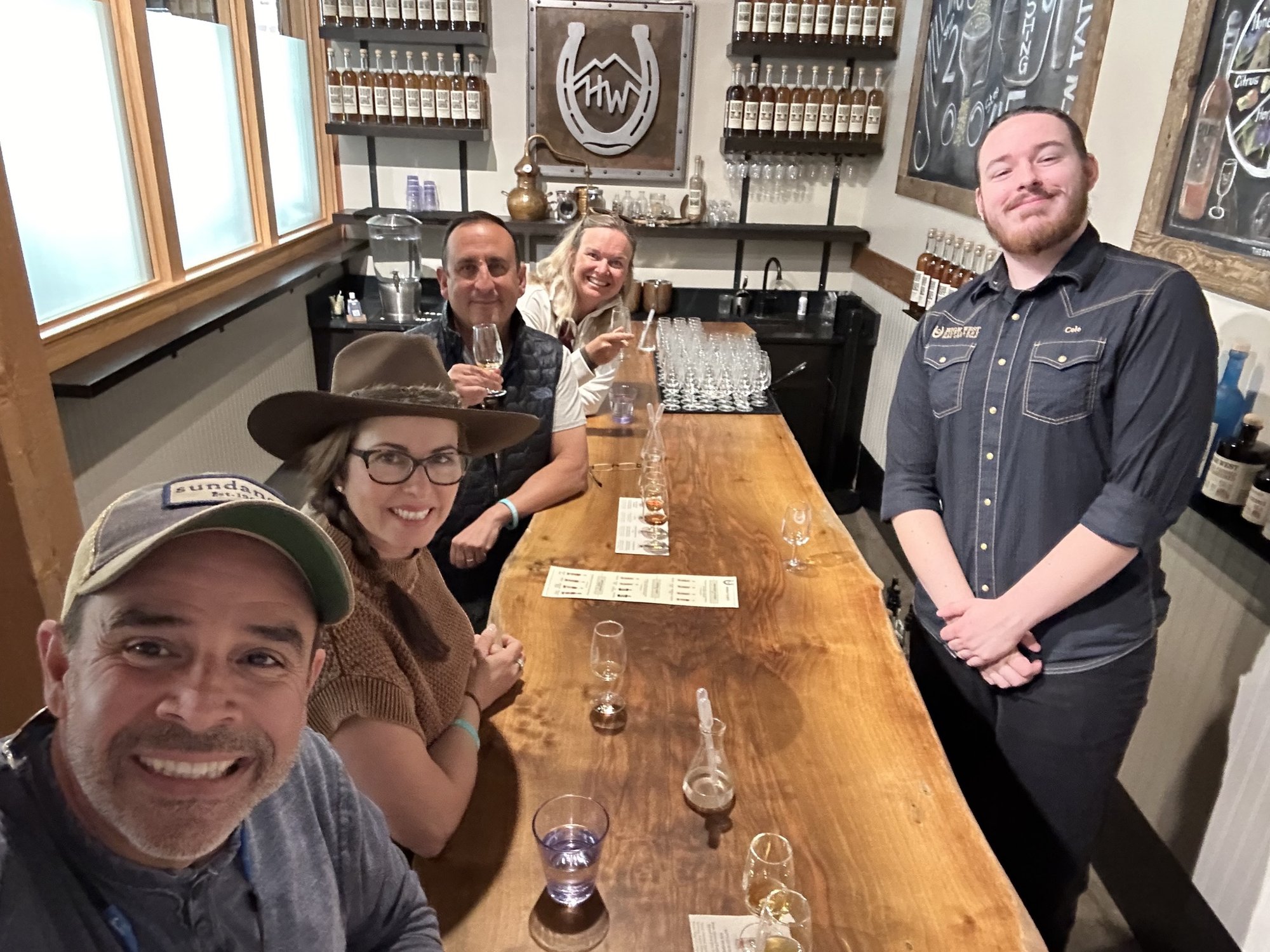 He-Stache, She-Stache and two friends smiling around a long live-edge tasting bar at High West, with their guide standing at the end