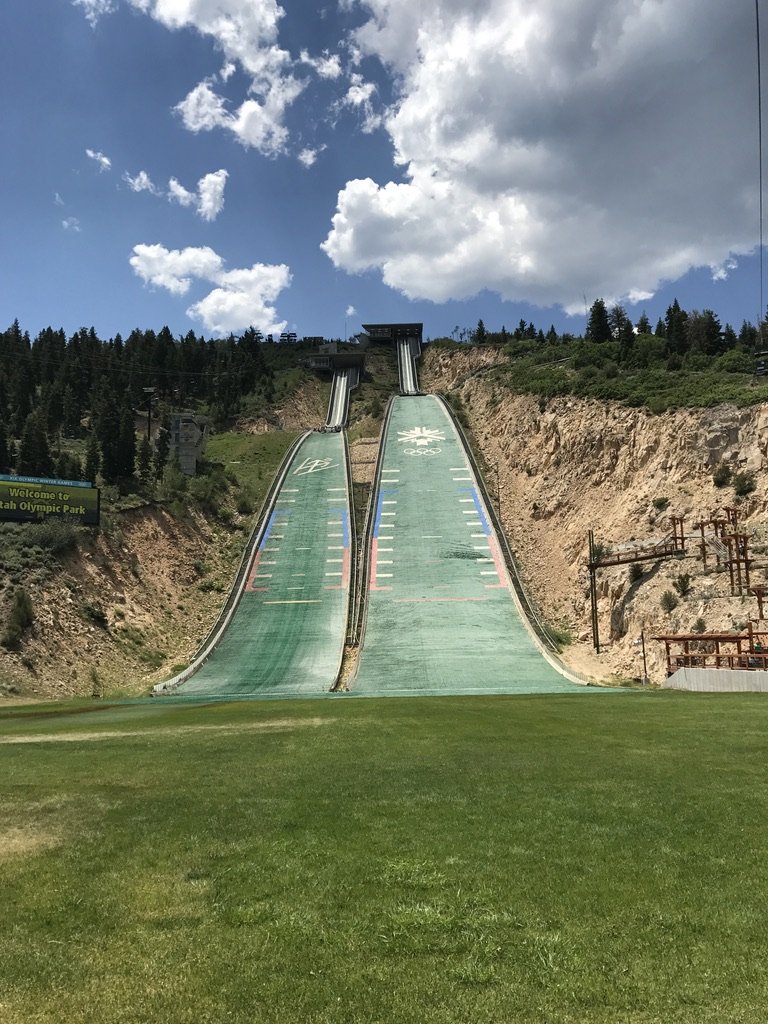 The green summer landing hills of the Olympic ski jumps at Utah Olympic Park under a blue sky with big clouds