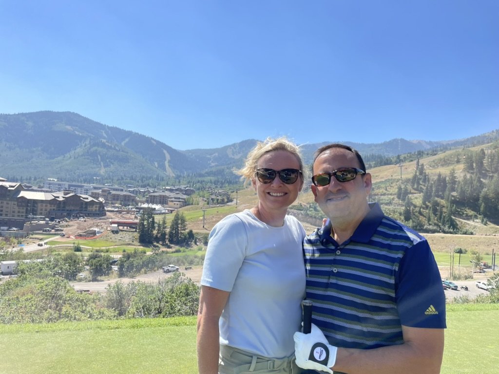 She-Stache and He-Stache on a tee box at Canyons Golf, with Canyons Village and construction cranes in the valley behind them