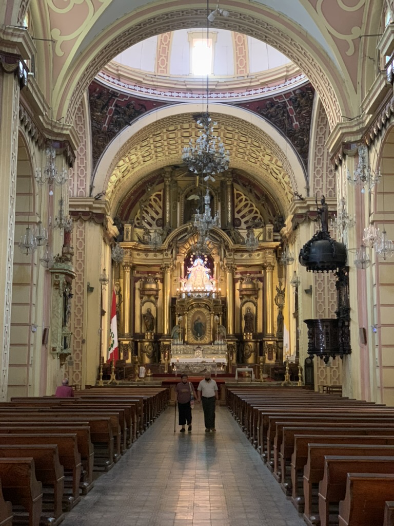 A colonial church interior with a gilded altar, chandeliers and a long central aisle