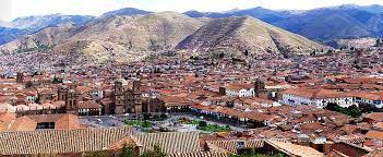 Red tile rooftops of Cusco with a church tower and brown mountains behind