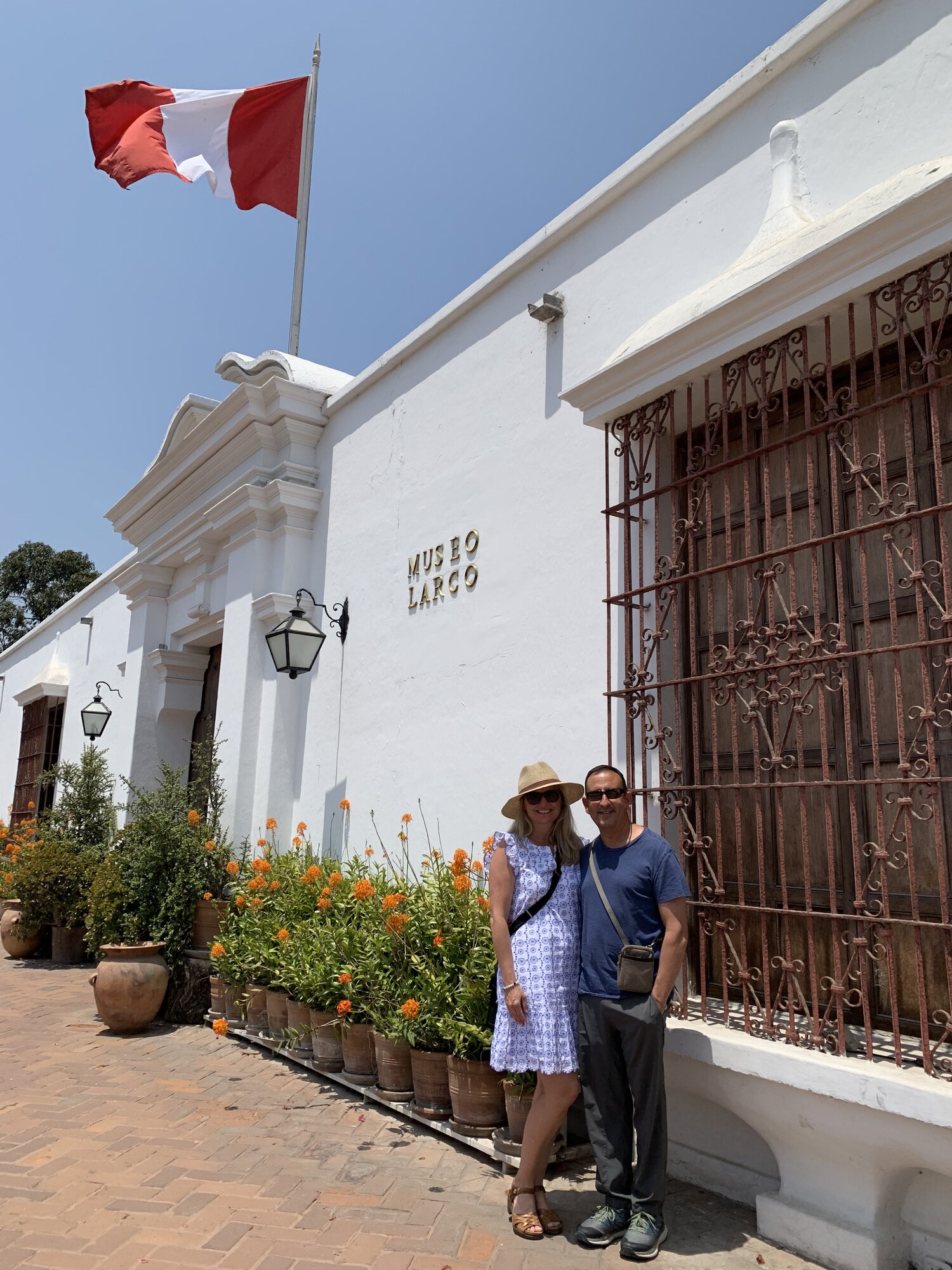 She-Stache and He-Stache outside the white-walled Larco Museum beside a Peruvian flag