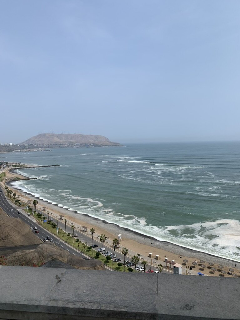 A wide beach and coastal road curving along the cold Pacific in Lima