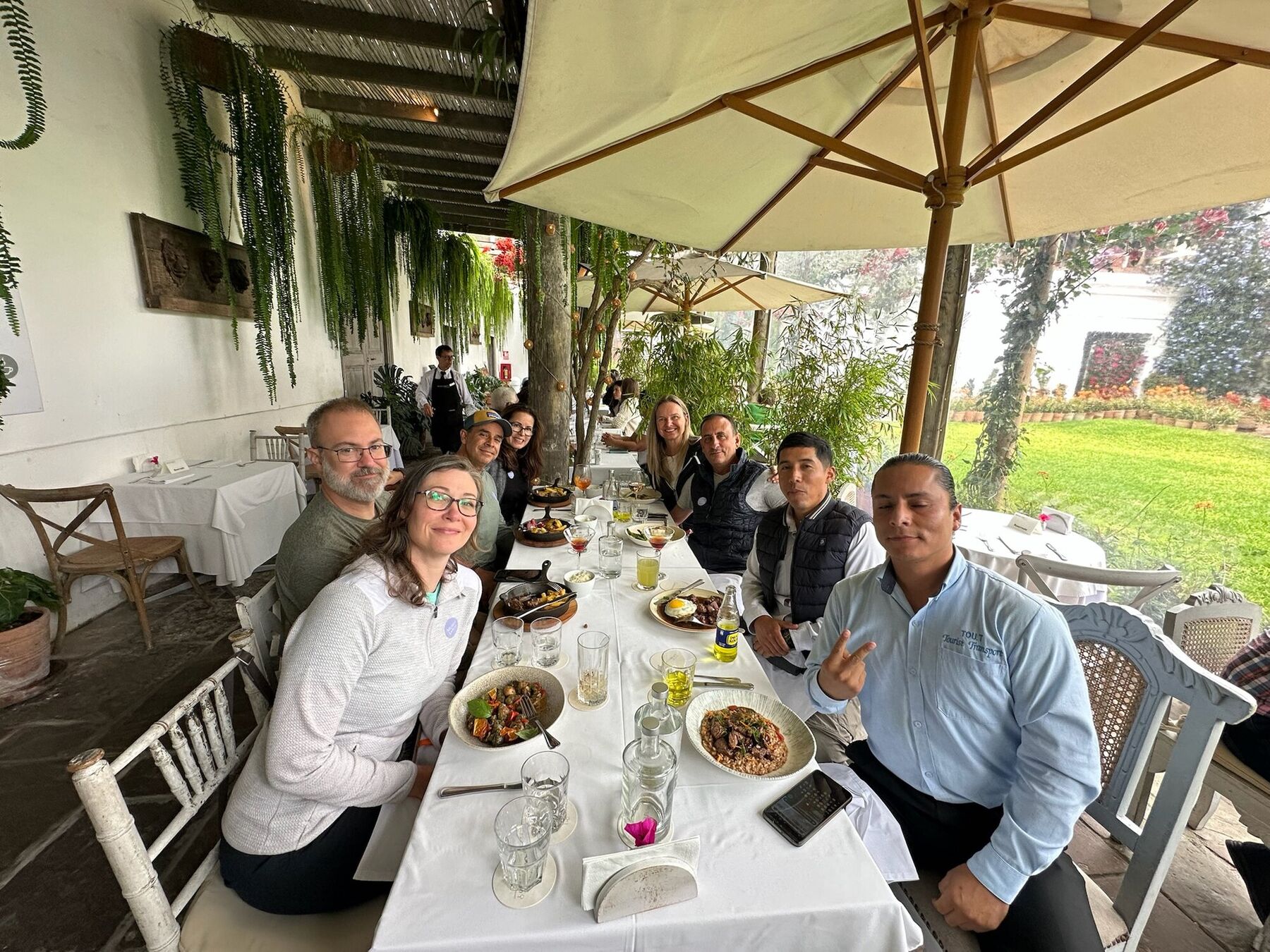 A long table of friends and guides lunching on a covered terrace overlooking a garden in Lima
