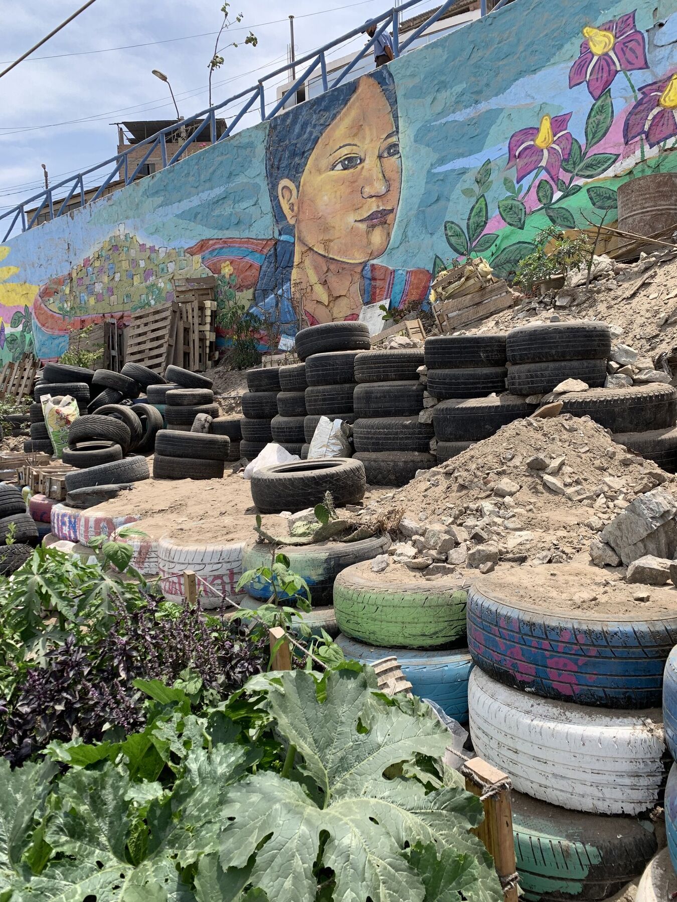 Garden terraces built from old tires on a Lima hillside beneath a painted mural