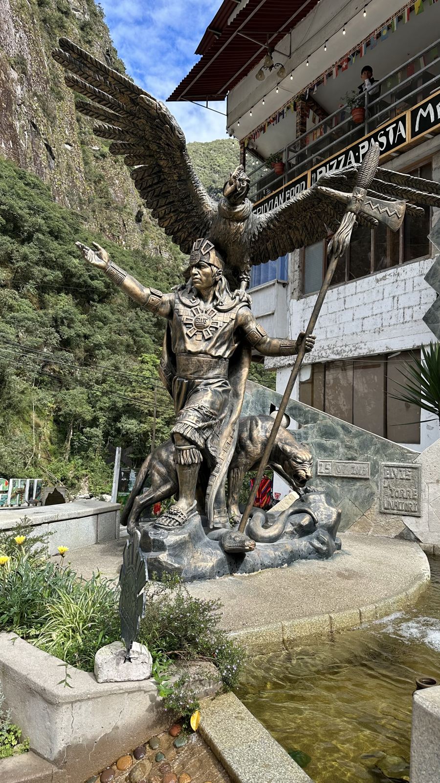A bronze statue of a winged figure beside a stone building