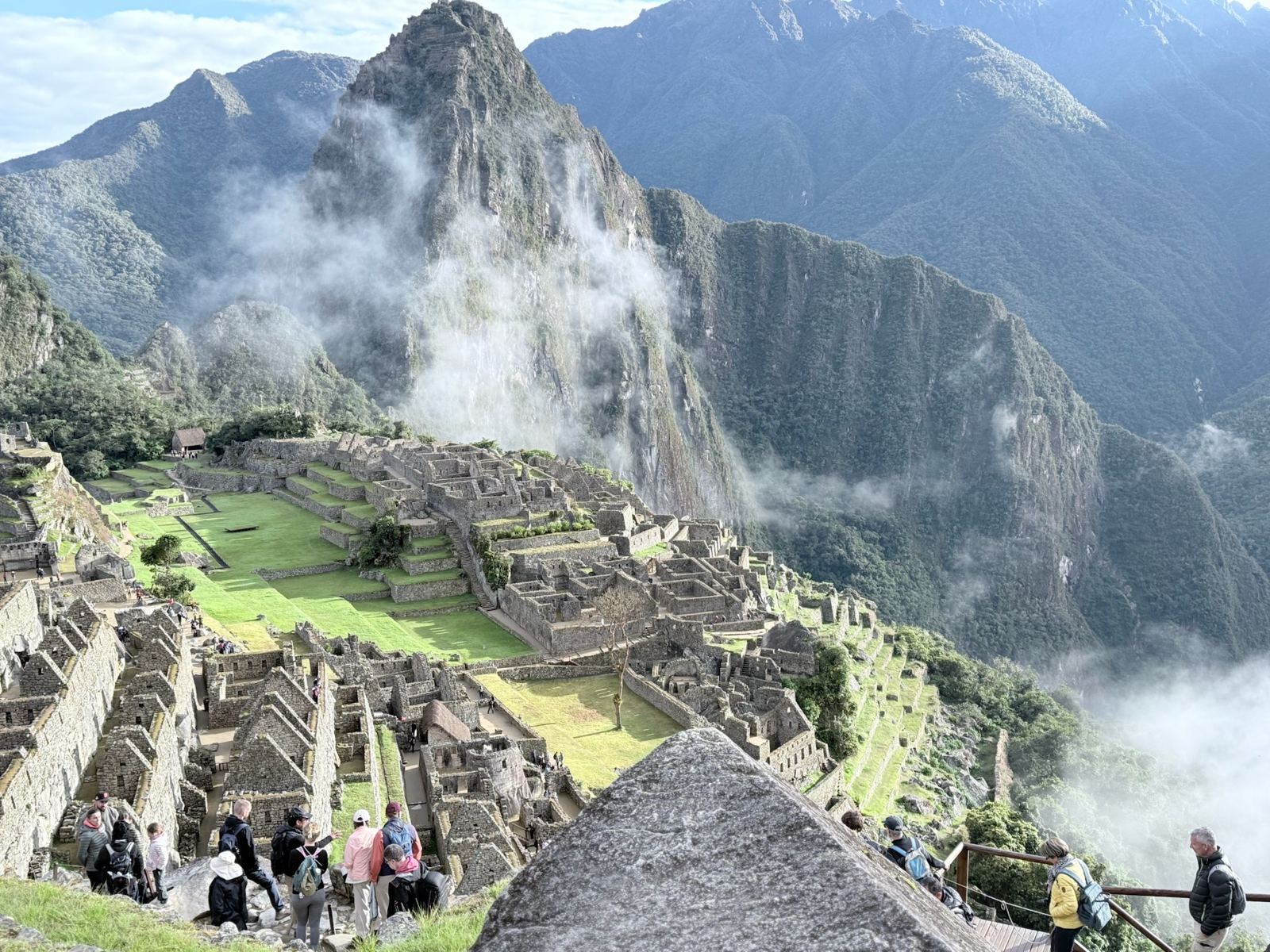 Visitors lining the terrace edge above the ruins as clouds drift through