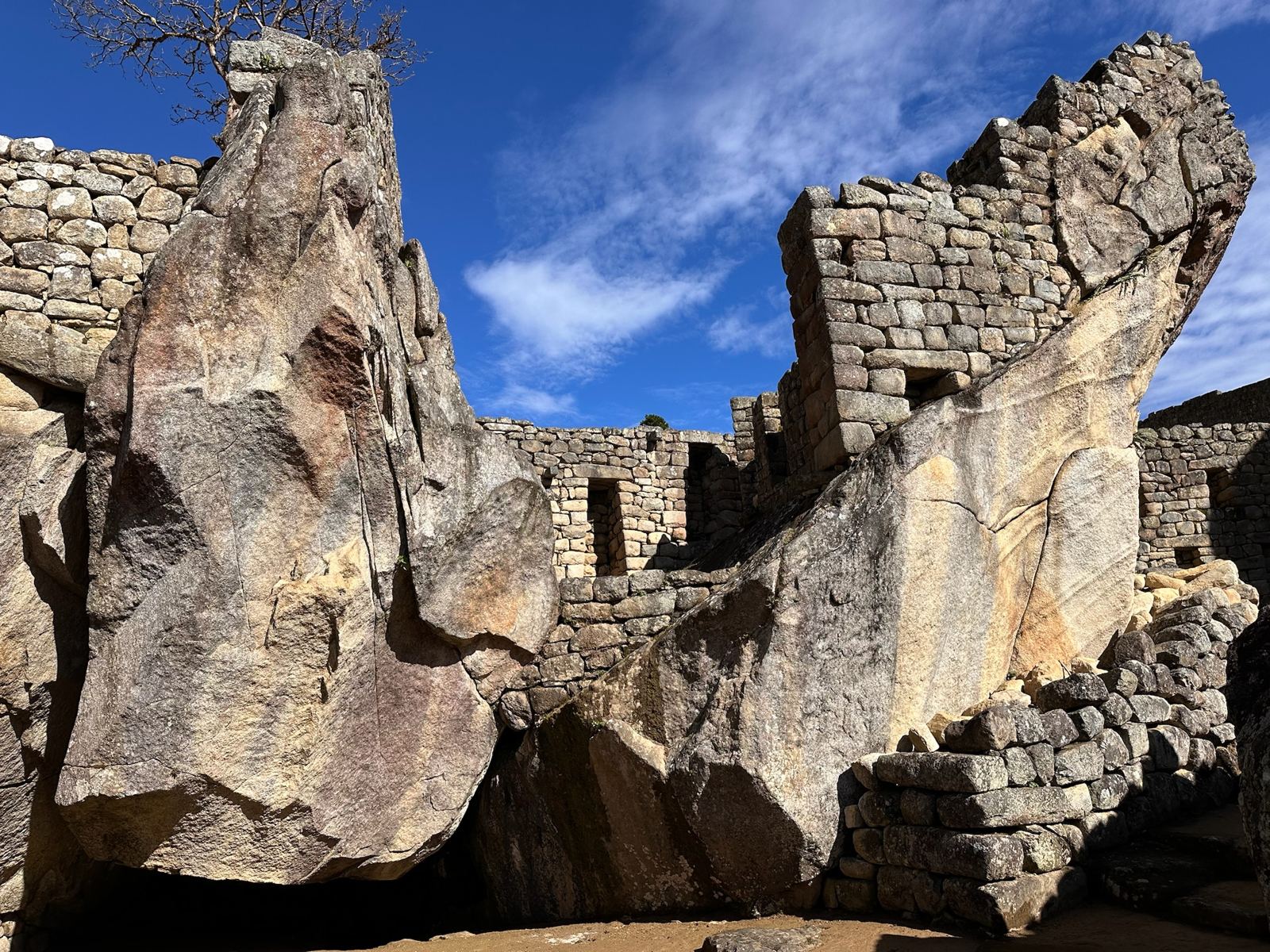 A carved boulder beside fitted stone walls under a deep blue sky