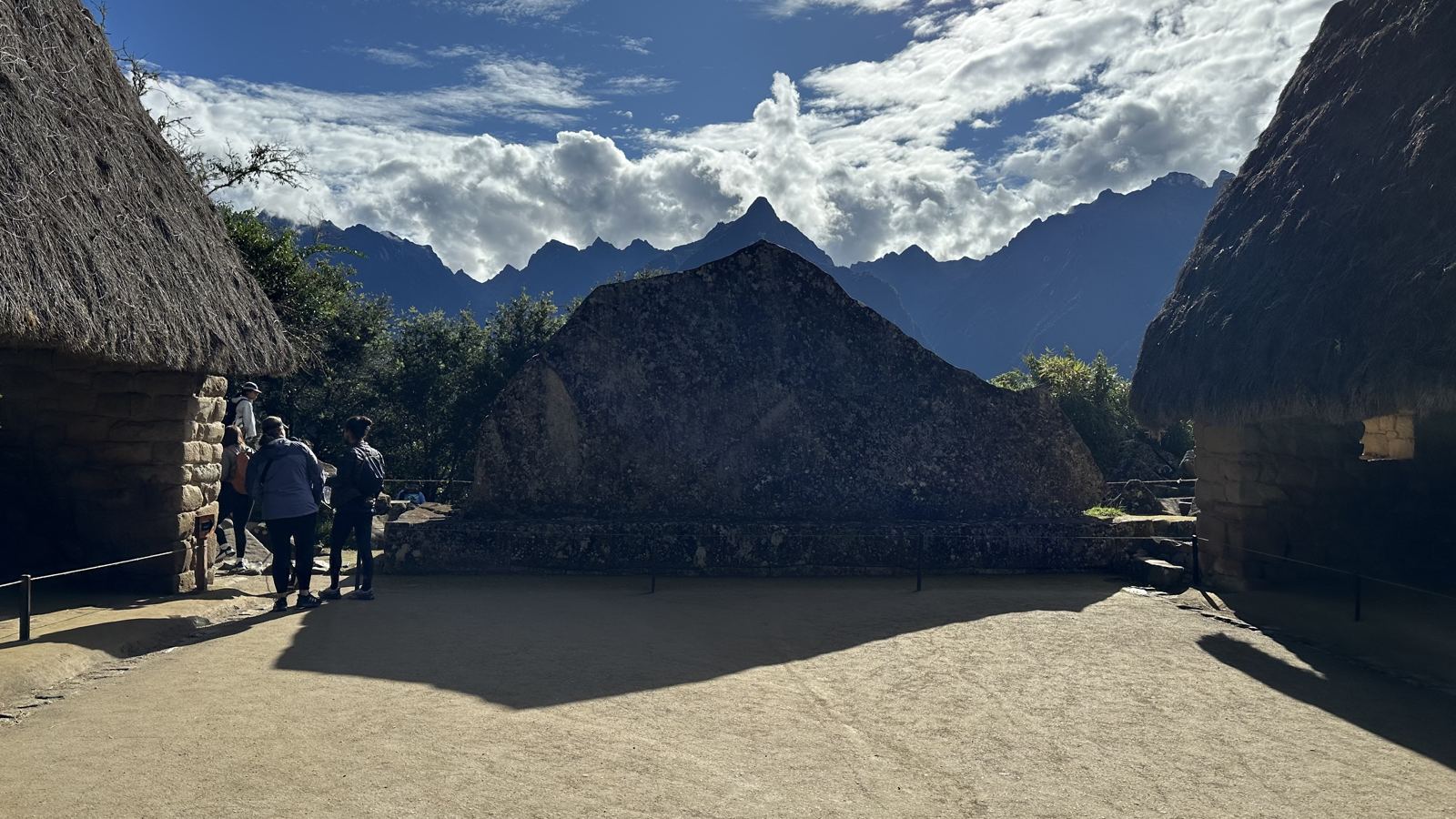 A large sloped stone between two thatched huts, with the mountains behind
