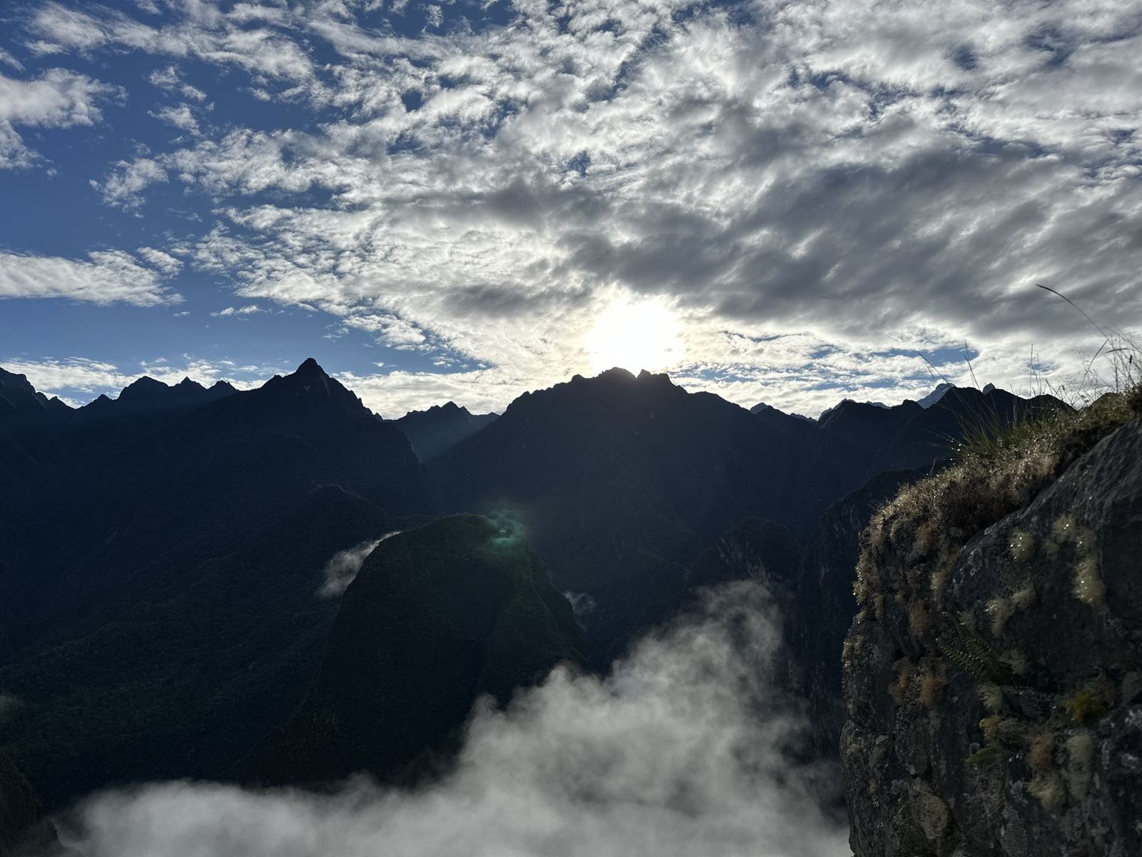 The sun breaking over a dark ridge, with clouds filling the valley below