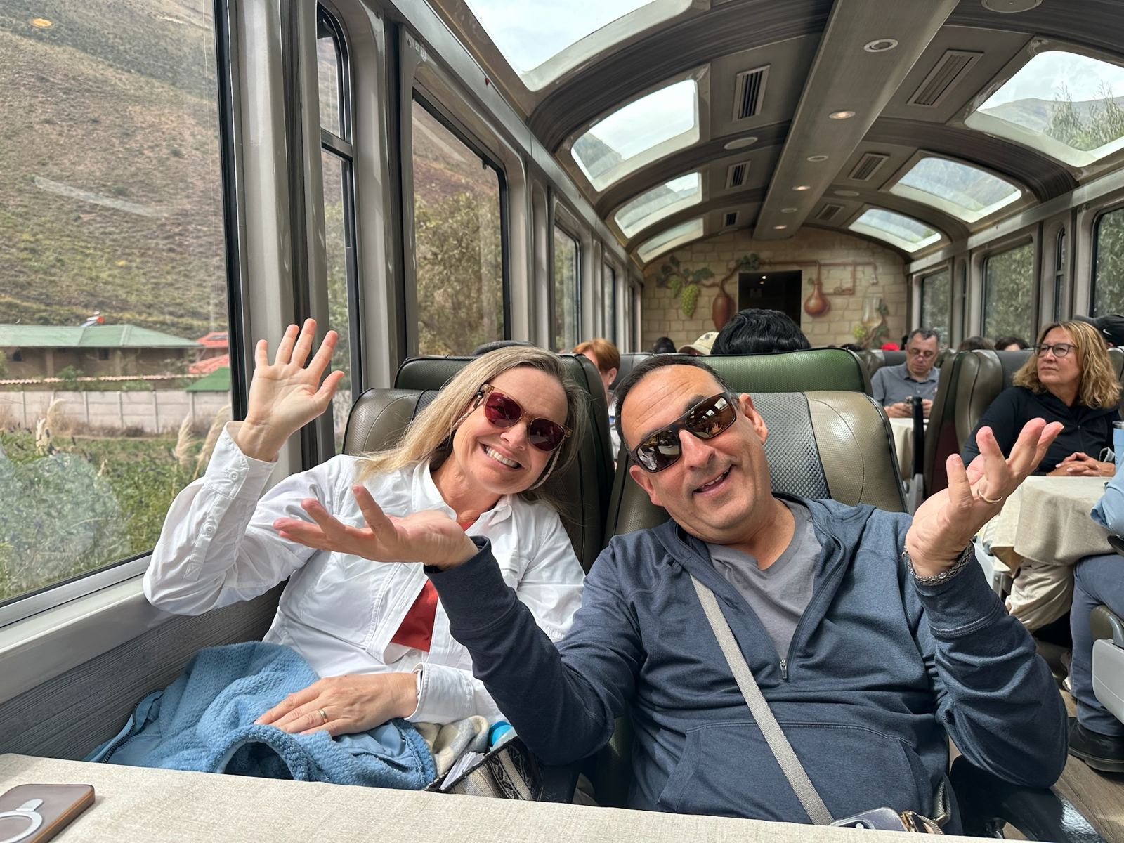 She-Stache and He-Stache waving from seats in a panoramic train car