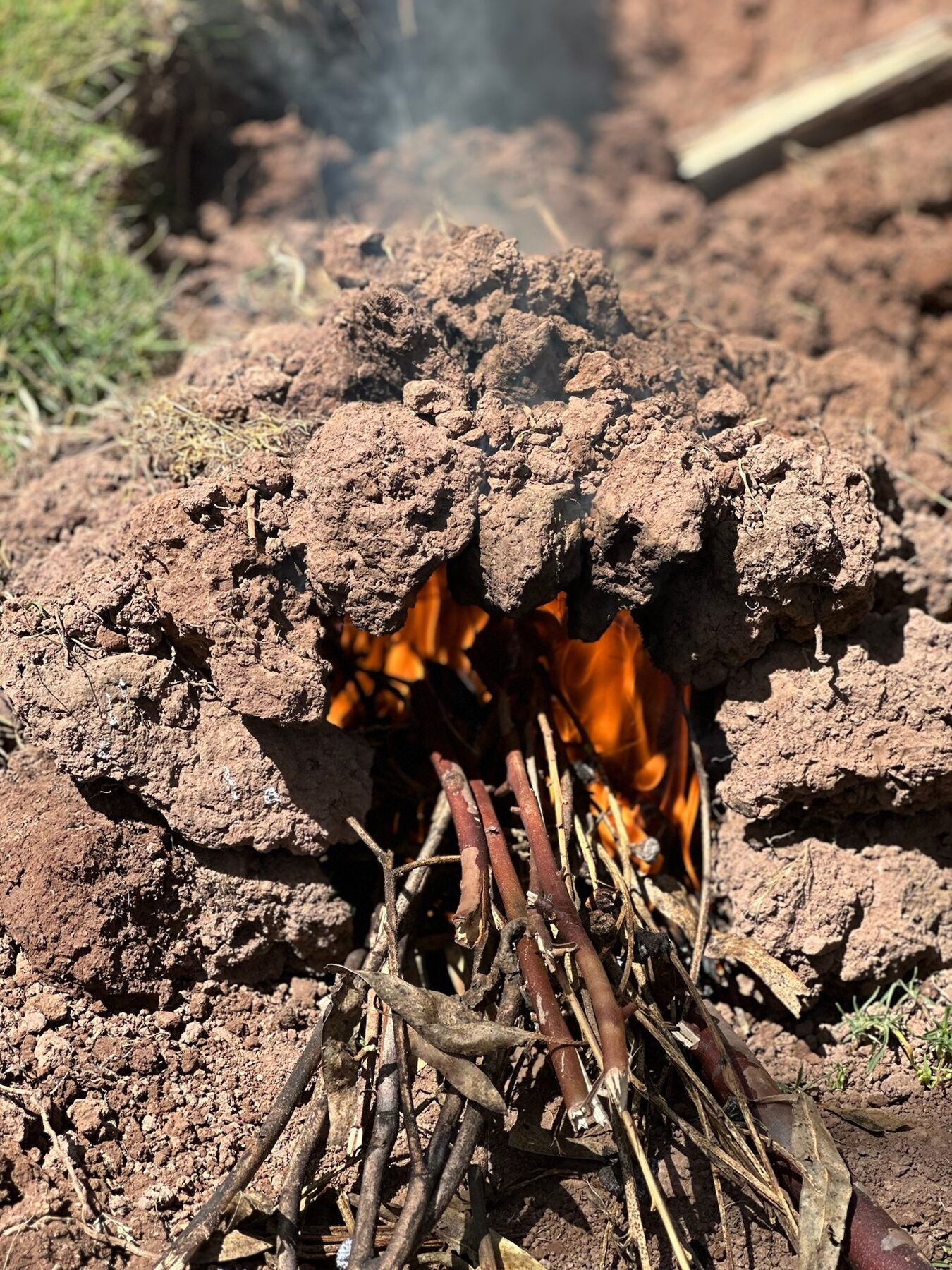 A smoking earth oven made of clods of dirt with a wood fire burning inside