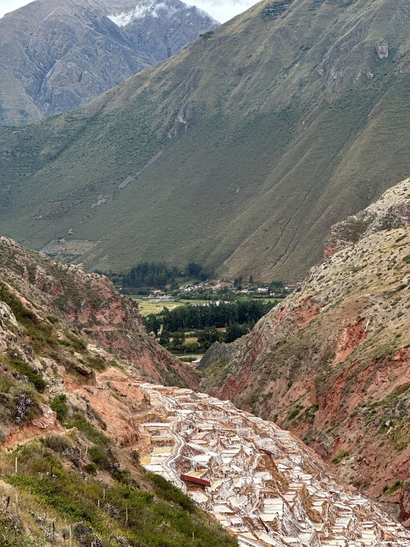 The Maras salt pools spilling down a narrow red-rock gorge toward the green valley floor