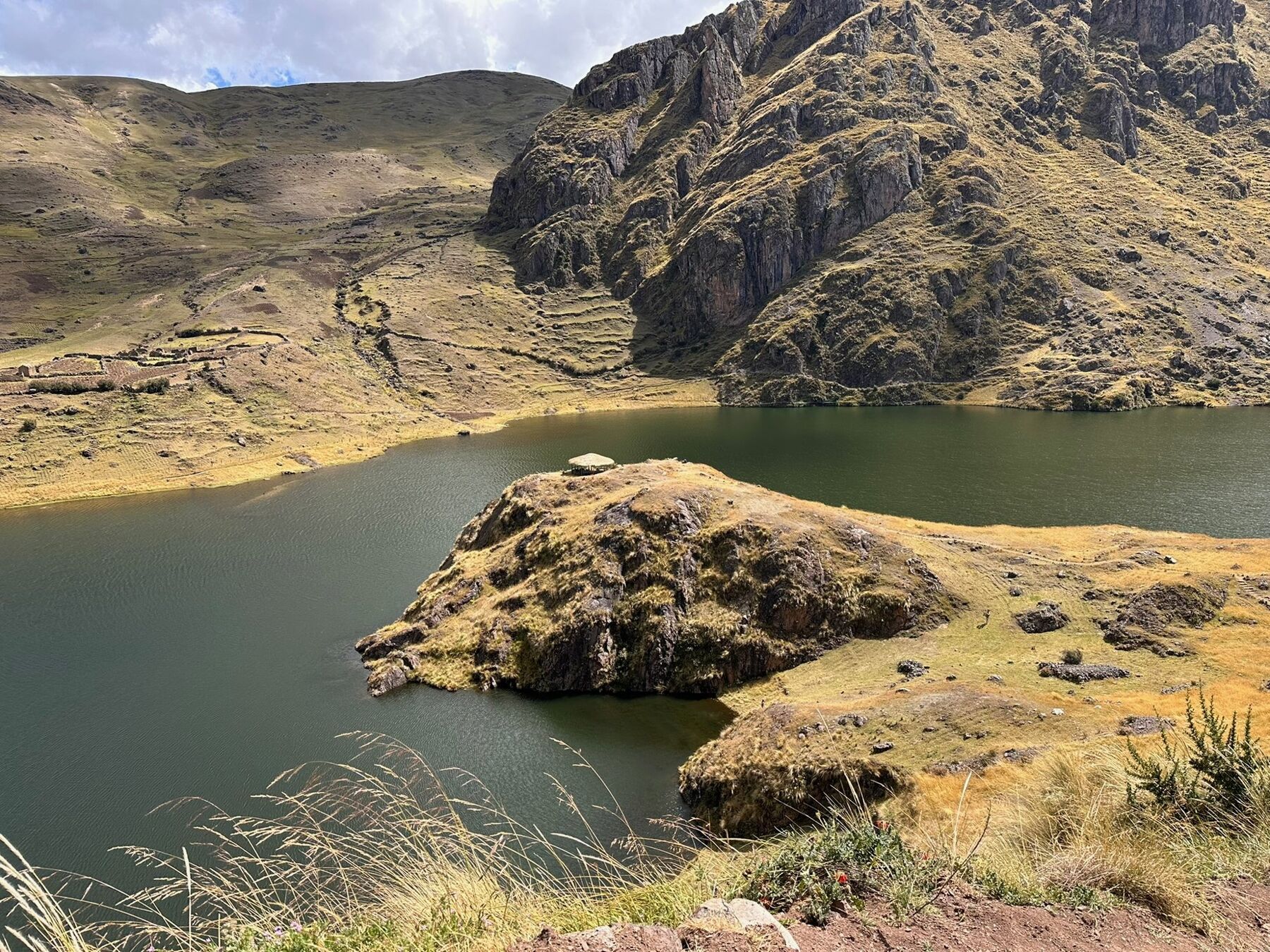 A dark green high-altitude lake with a small thatched shelter on a rocky point