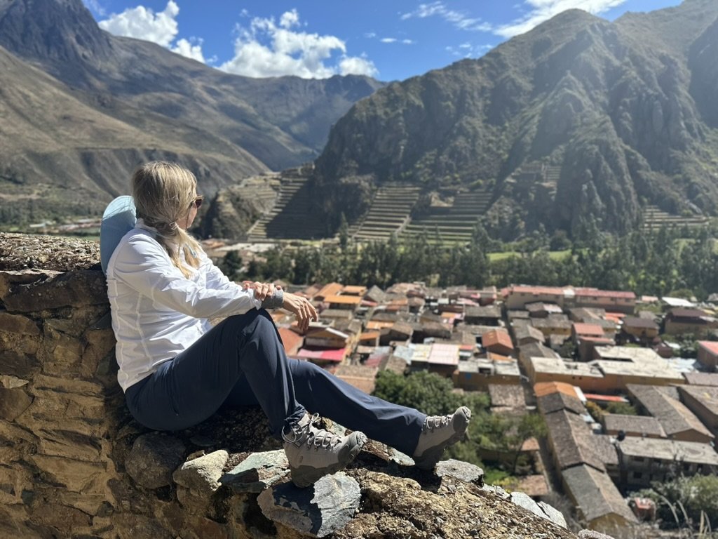 She-Stache sitting on a stone wall above a Sacred Valley town, with mountains behind