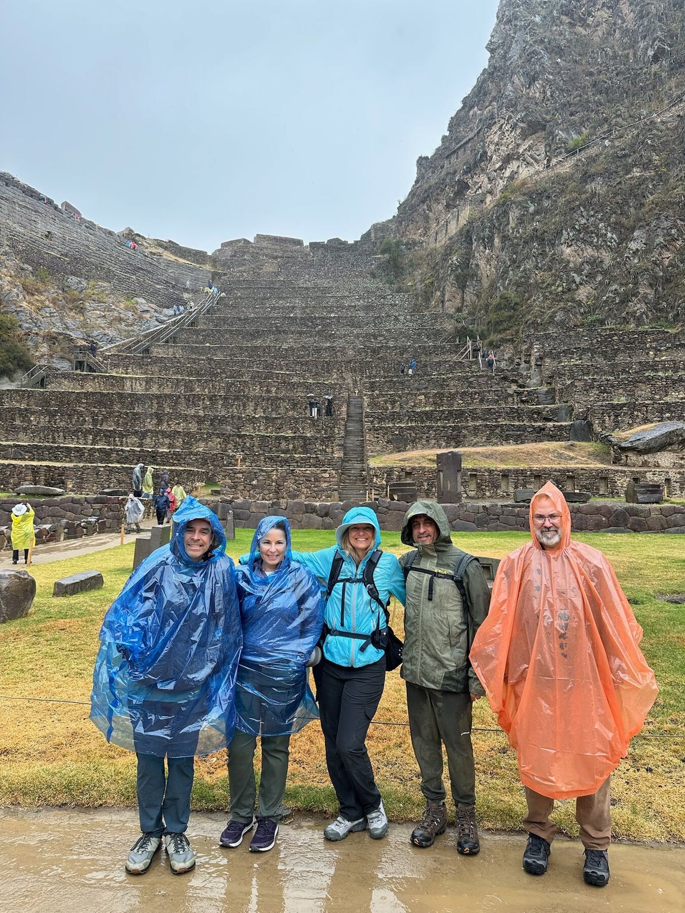 Five travelers in rain ponchos and jackets in front of the steep stone terraces of Ollantaytambo