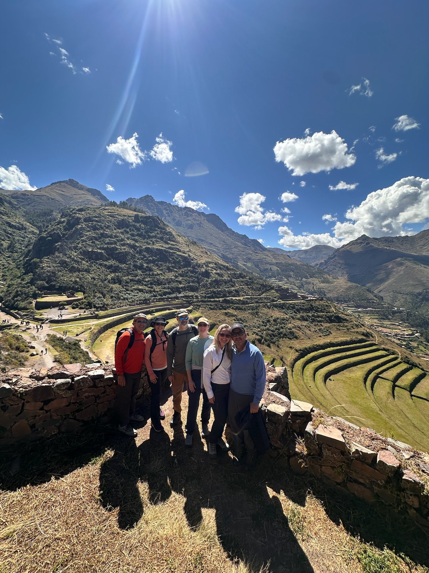 The six travelers posing on a stone wall above the curved agricultural terraces of Pisac