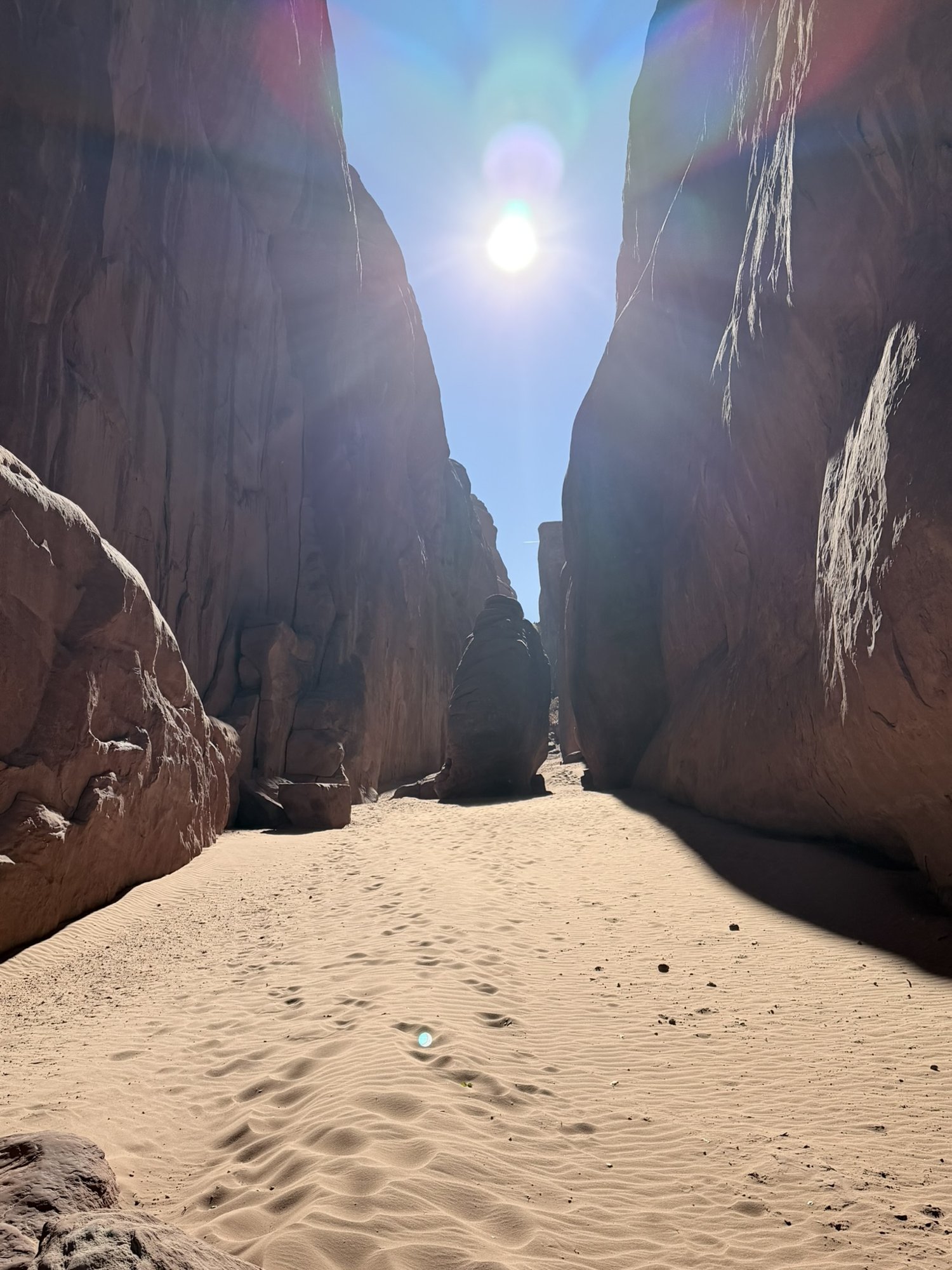 A sunlit corridor of soft sand between sandstone walls near Sand Dune Arch
