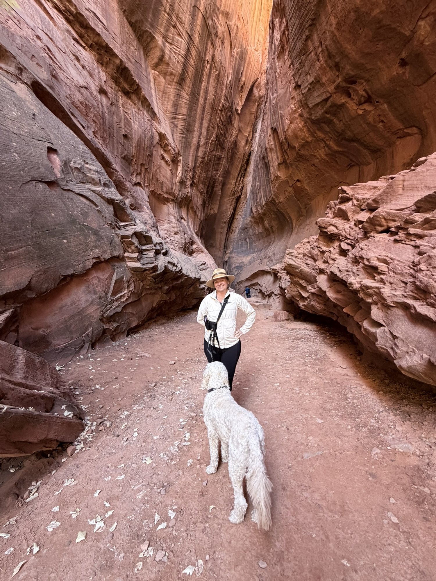 She-Stache standing in a sandy slot canyon off the Burr Trail while Pup-Stache, seen from behind, looks up at her