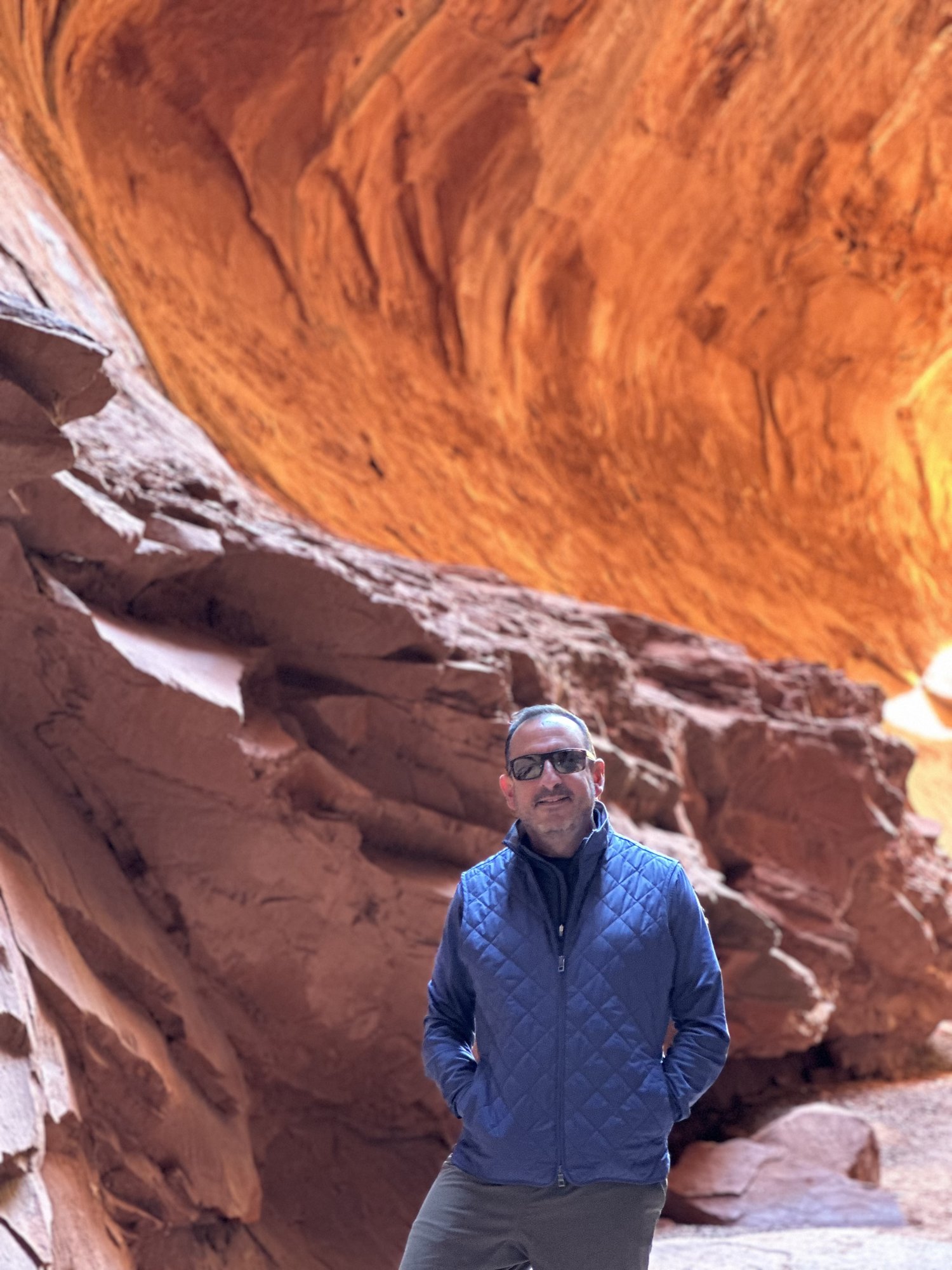 He-Stache standing under a sweeping orange sandstone overhang in the Escalante canyon country
