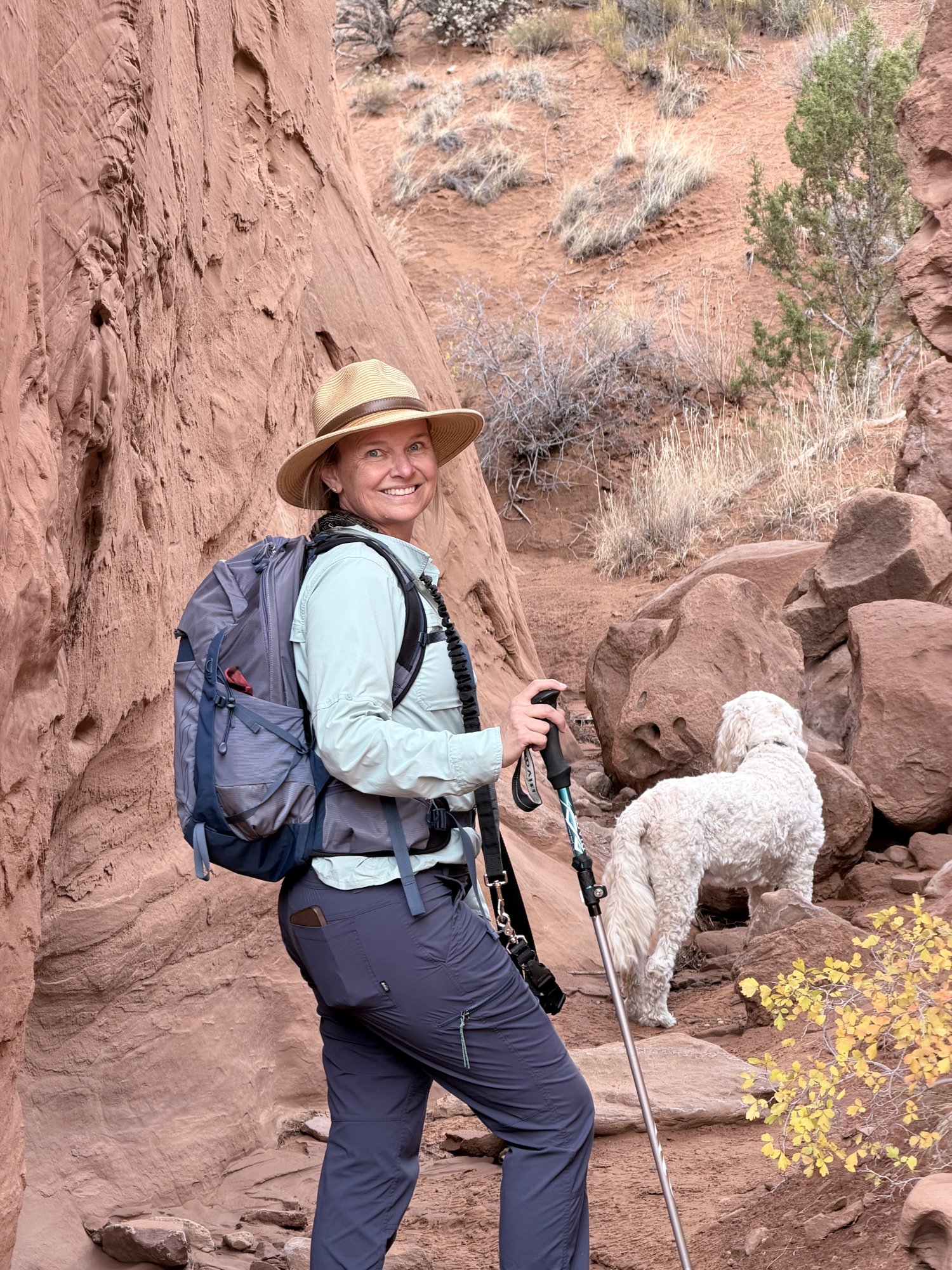 She-Stache smiling back at the camera on a rocky canyon trail while Pup-Stache sniffs ahead