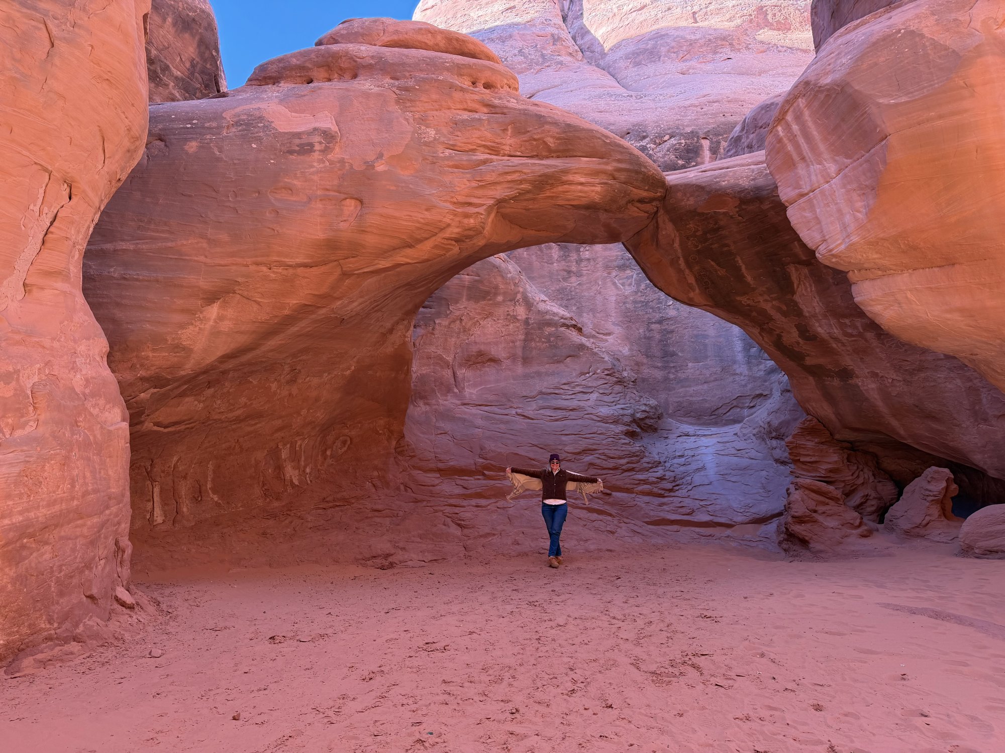 She-Stache standing with arms outstretched under Sand Dune Arch in Arches National Park