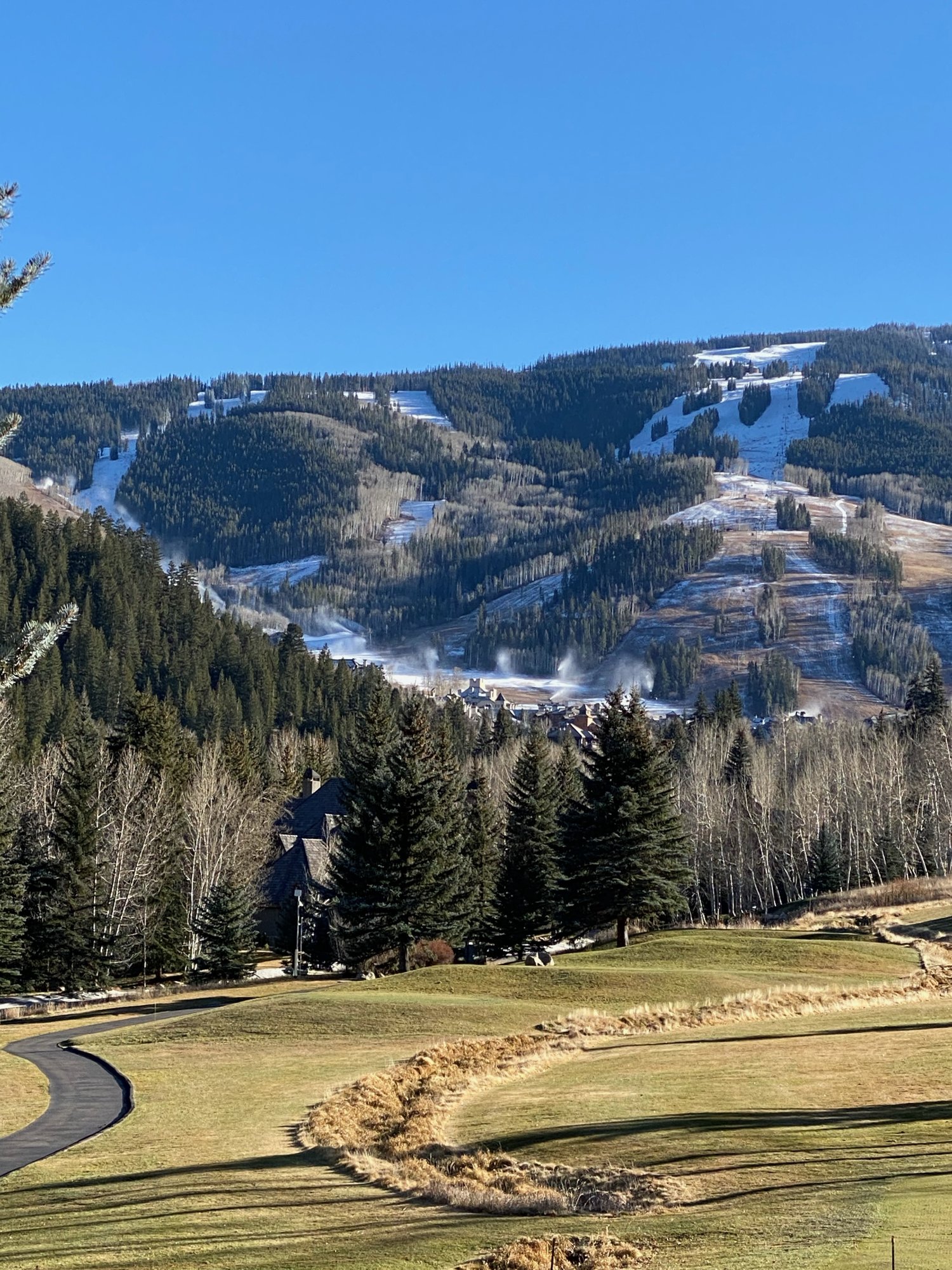 Beaver Creek Mountain seen from Avon in late November, narrow white strips of man-made snow on the ski runs above a brown golf course