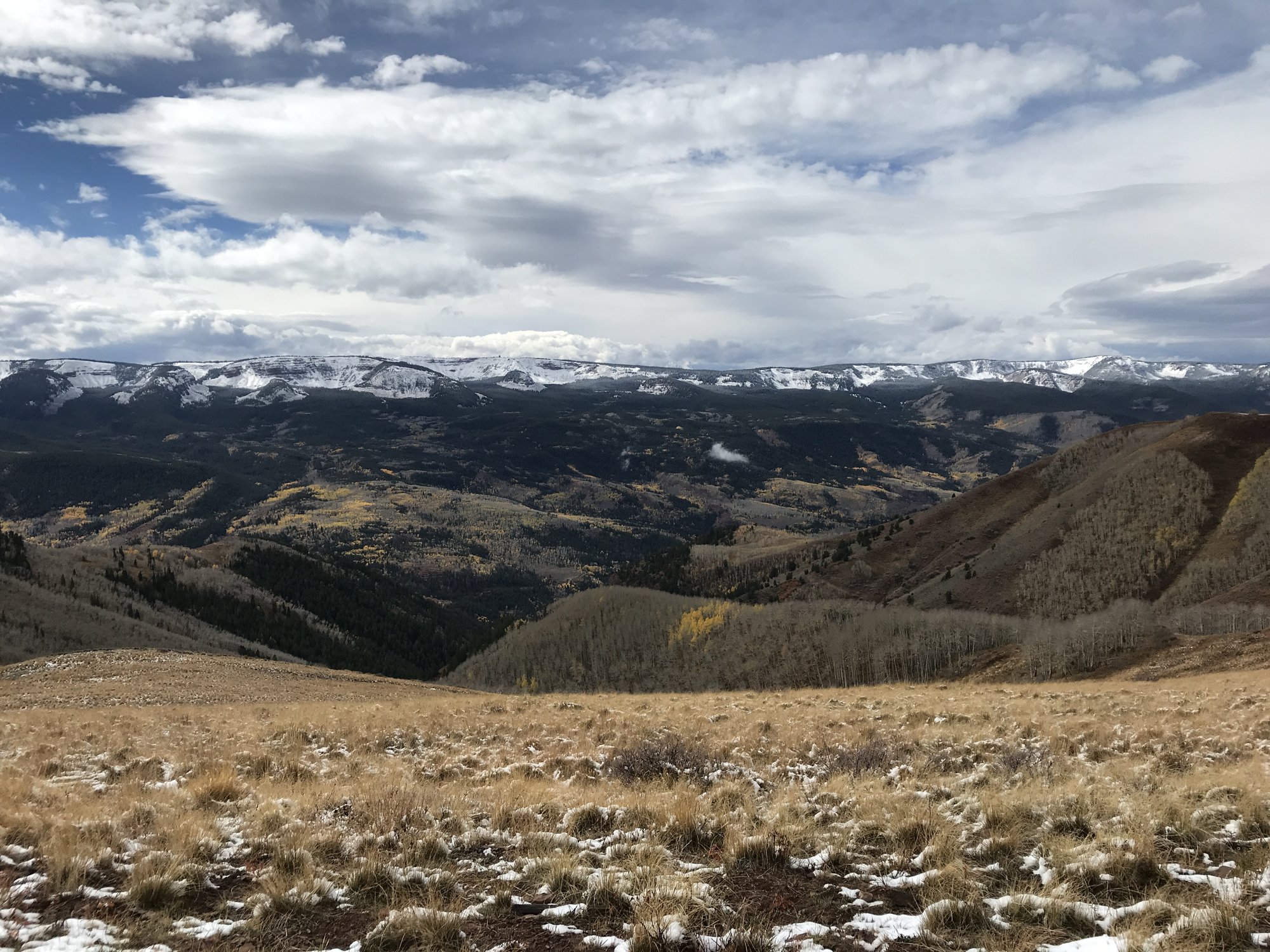A wide high-country meadow of dry grass with snow-capped ranges on the horizon