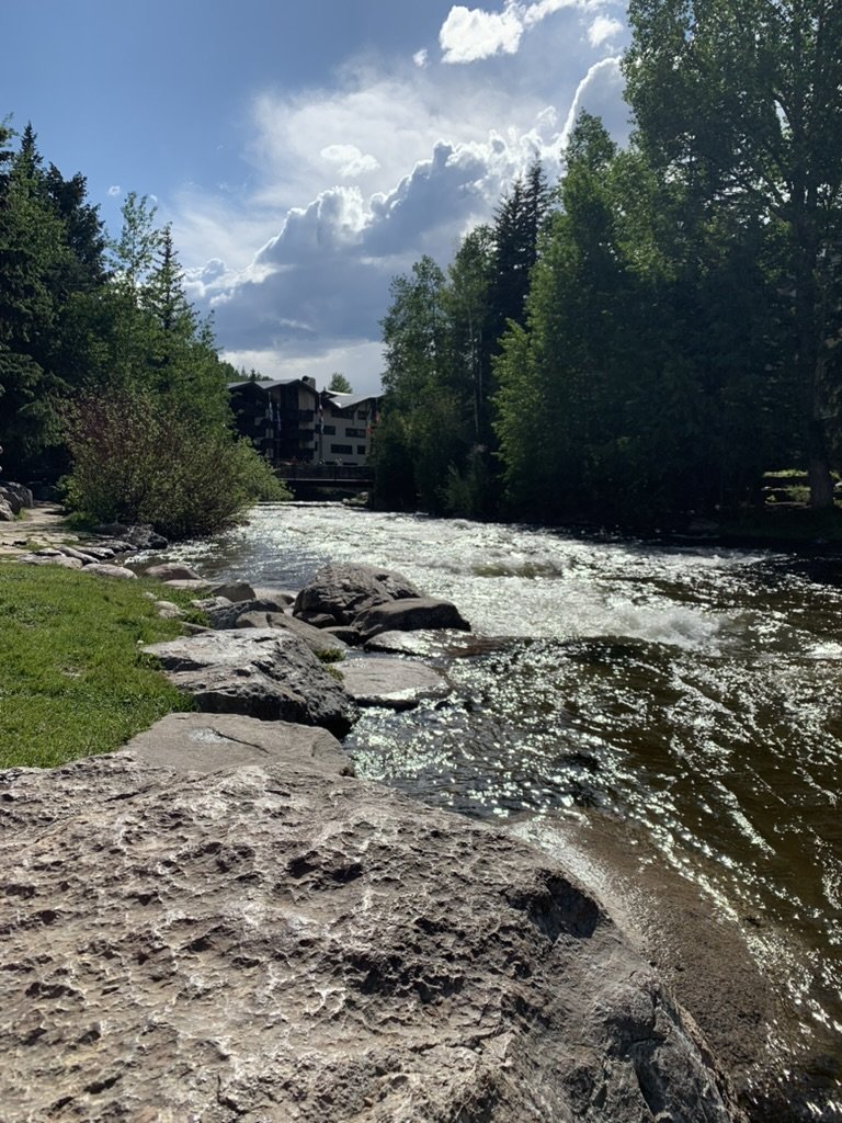 Gore Creek running fast and sparkling over boulders through Vail, evergreens on both banks and a lodge behind under a big sky
