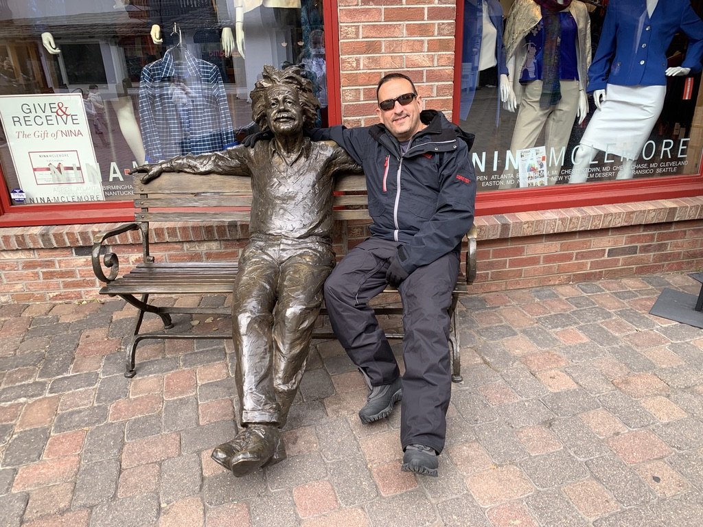He-Stache in ski pants on a bench with his arm around a bronze statue of Albert Einstein, outside a shop in Vail Village