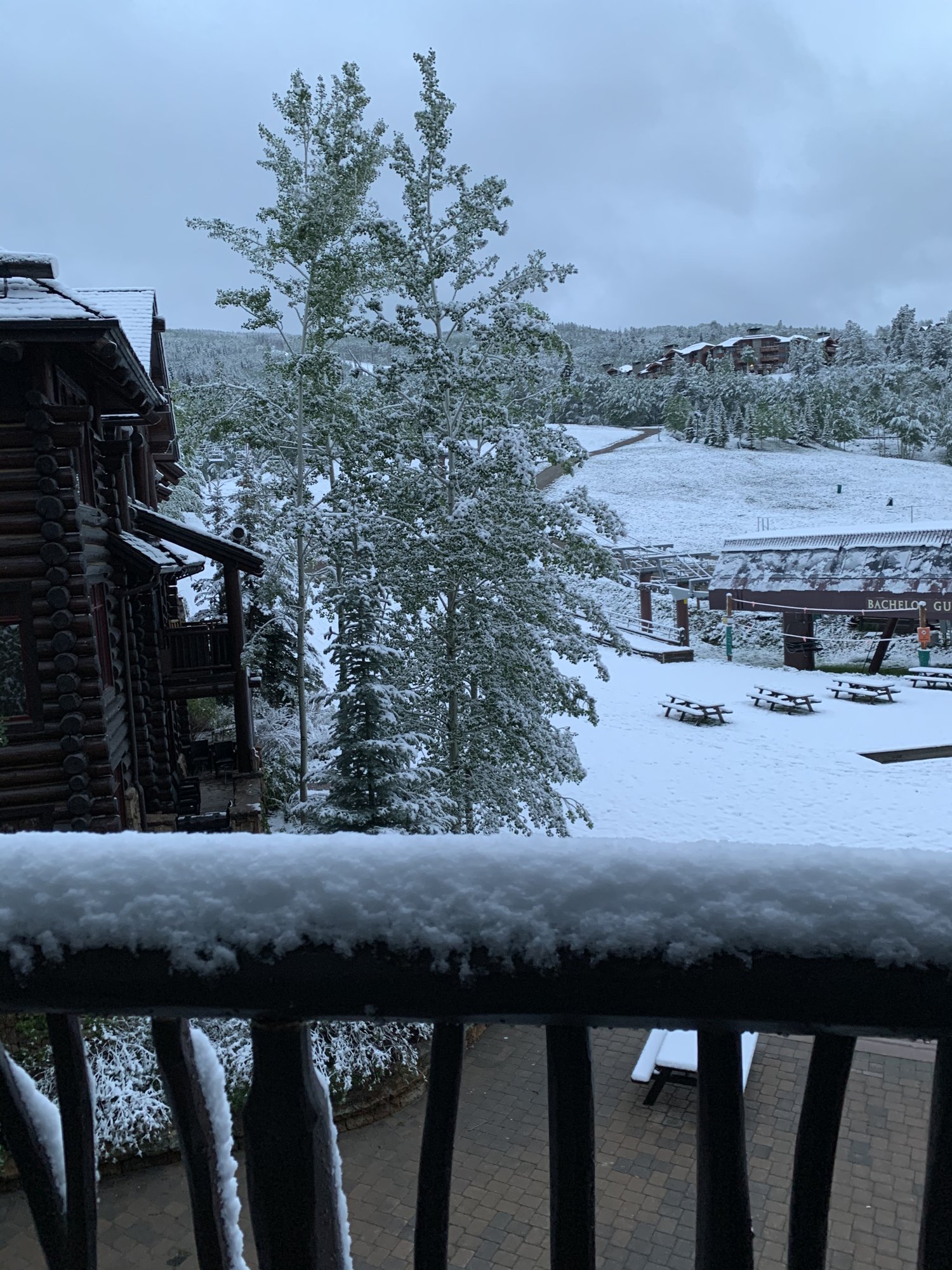 Fresh snow covering a balcony railing, evergreens and an empty lift base in Bachelor Gulch