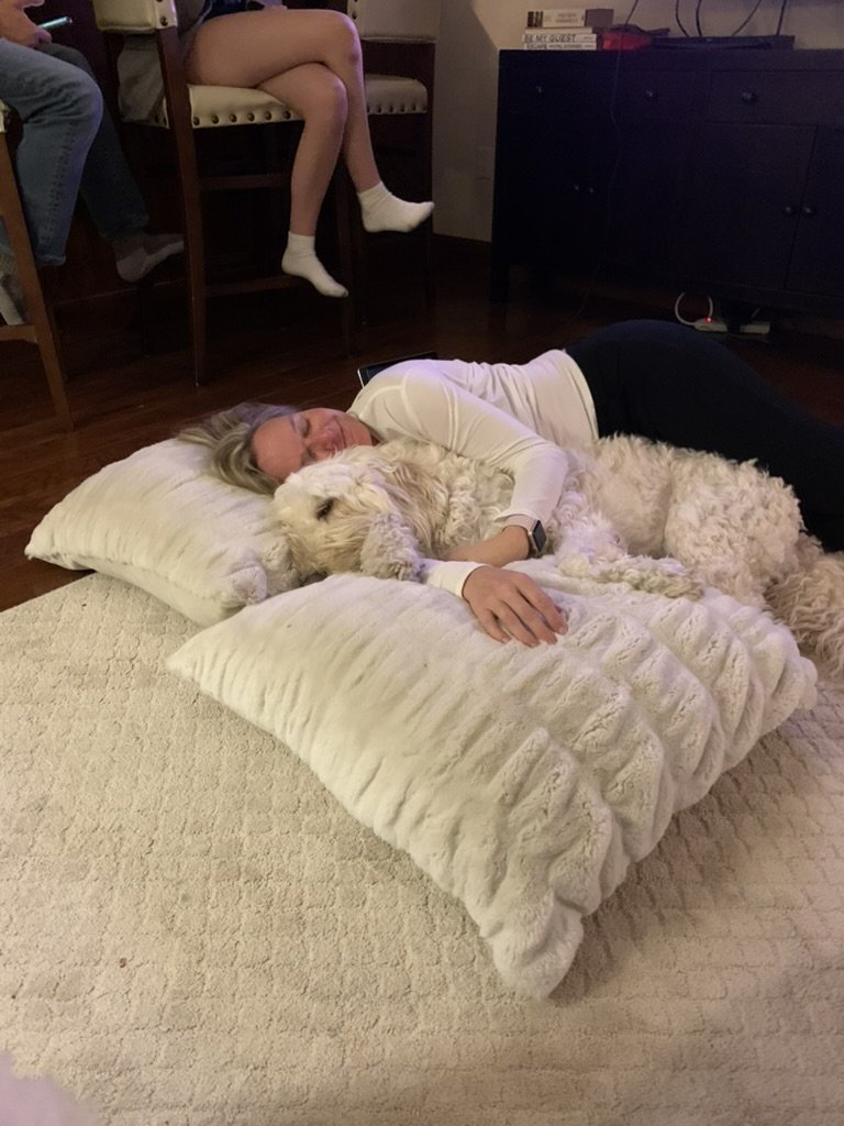 She-Stache lying on large white floor pillows hugging a sleepy Pup-Stache at the Ritz-Carlton Club, Vail