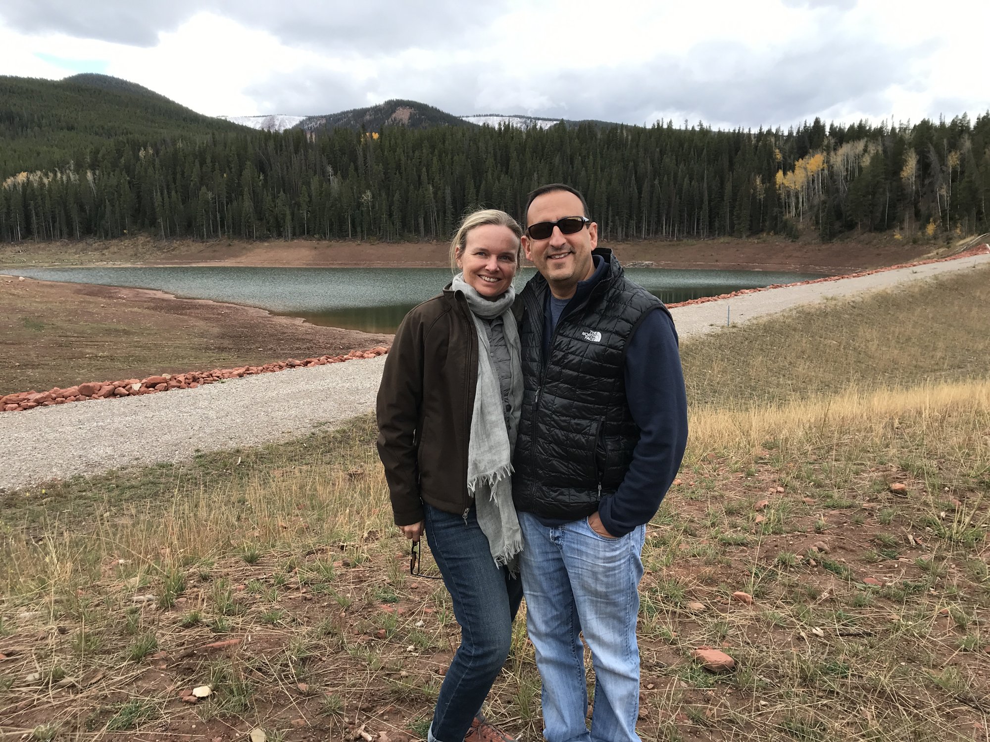 She-Stache and He-Stache posing on a dry hillside above a mountain lake and a dirt road in the Brush Creek valley