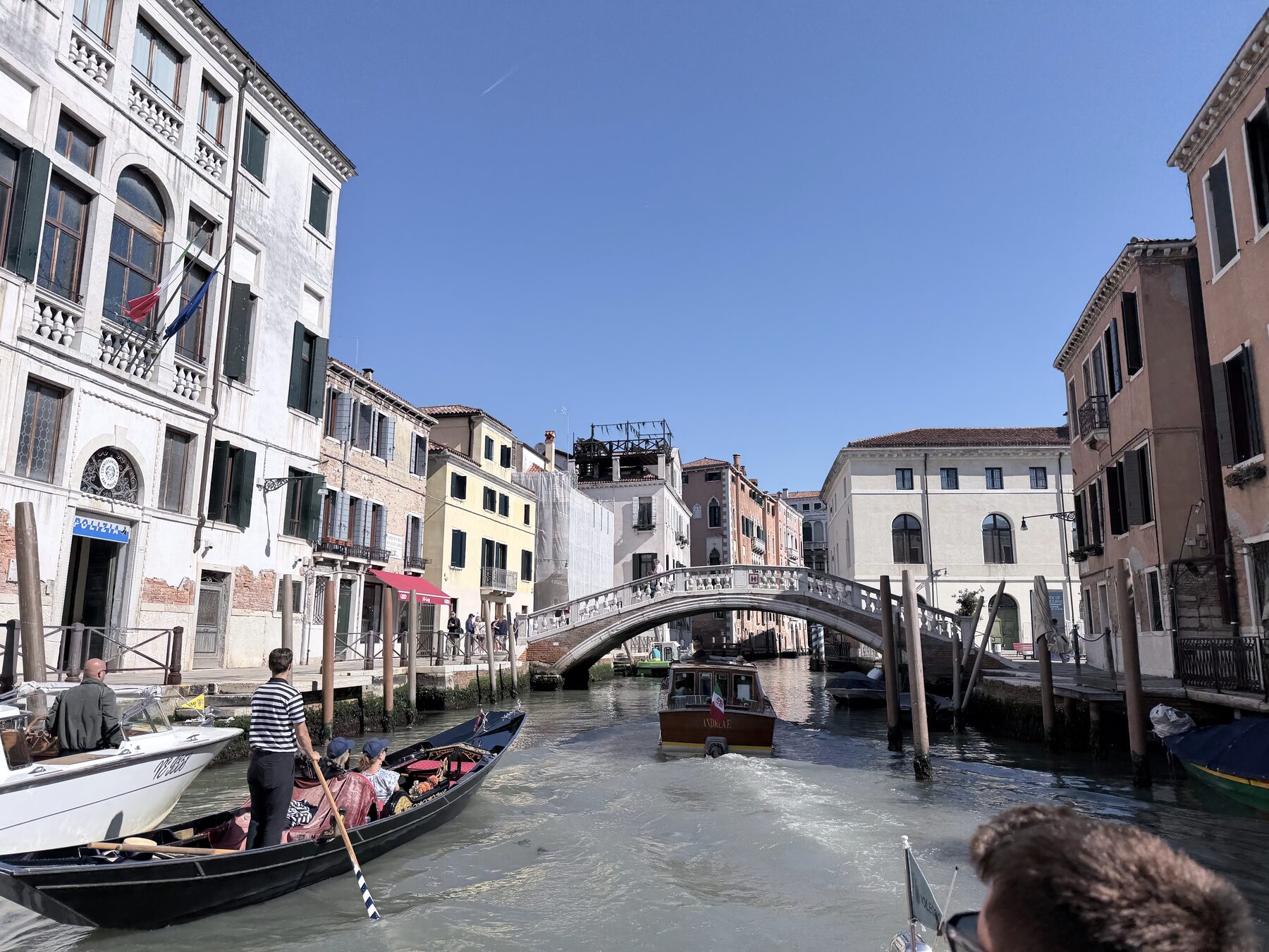 A quiet Venetian side canal lined with old buildings, a gondola passing under a small stone bridge